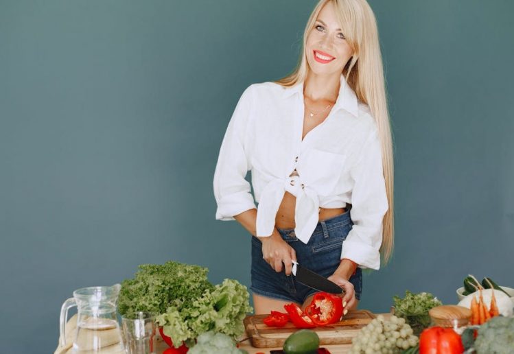 A smiling blonde woman chops vegetables, promoting healthy eating and lifestyle.