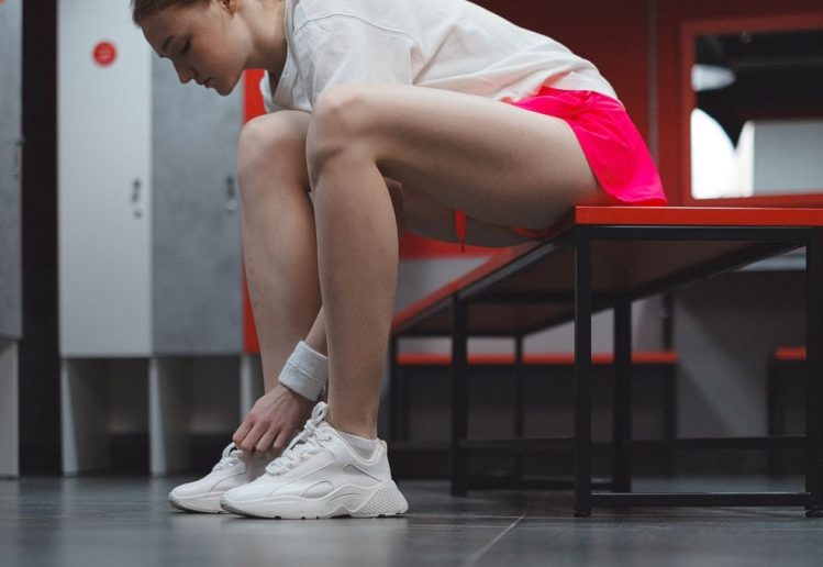 A woman in sportswear tying her shoes in a locker room, showing dedication to fitness.