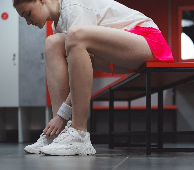A woman in sportswear tying her shoes in a locker room, showing dedication to fitness.