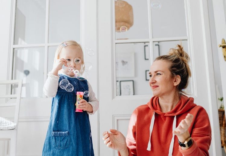 A joyful moment of a mother and daughter playing with bubbles indoors.