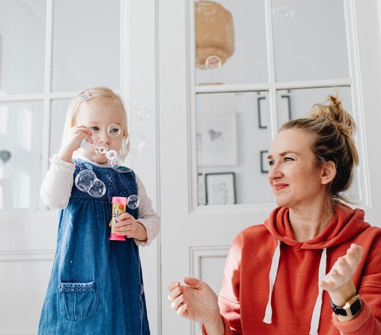 A joyful moment of a mother and daughter playing with bubbles indoors.